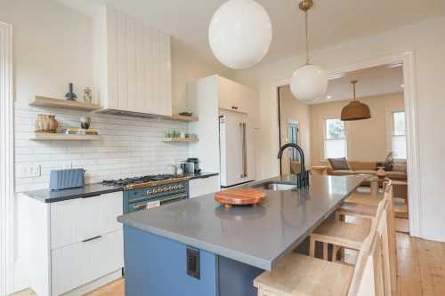 Modern kitchen featuring a large island, sleek cabinetry, and pendant lighting, with a cozy living area in the background.