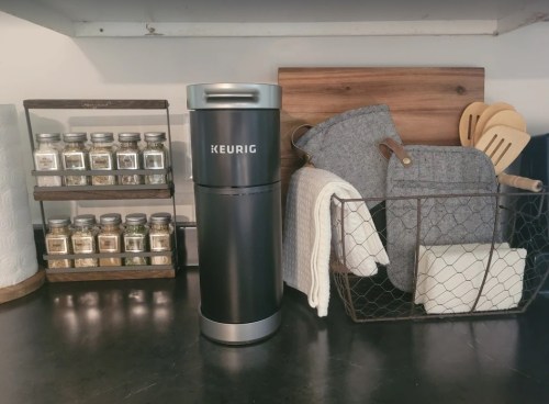 A Keurig coffee maker next to a spice rack, kitchen utensils, and storage containers on a countertop.