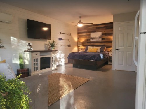 Cozy bedroom with a wooden accent wall, TV, and modern decor, featuring a bed, seating area, and natural light.