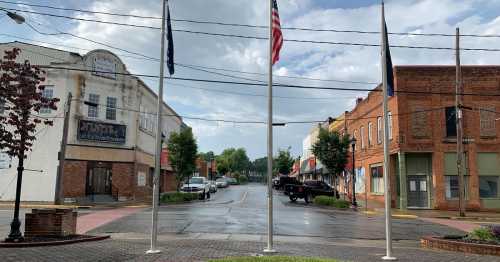 A quiet street scene with flags, shops, and wet pavement under a cloudy sky.