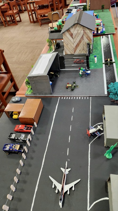 A colorful model city layout with buildings, vehicles, and an airplane on a runway, set on a library table.