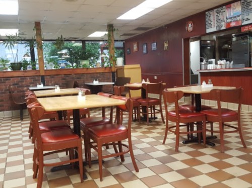 A cozy diner interior with red and brown checkered floors, empty tables, and plants near the windows.
