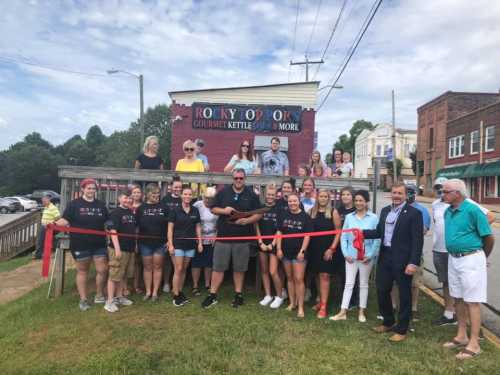 A group of people gathers for a ribbon-cutting ceremony outside Rocky Top Pop, celebrating the new gourmet kettle corn shop.