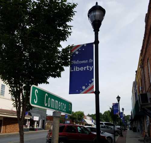 A street sign for S Commerce St with a "Welcome to Liberty" banner on a lamp post in a small town setting.