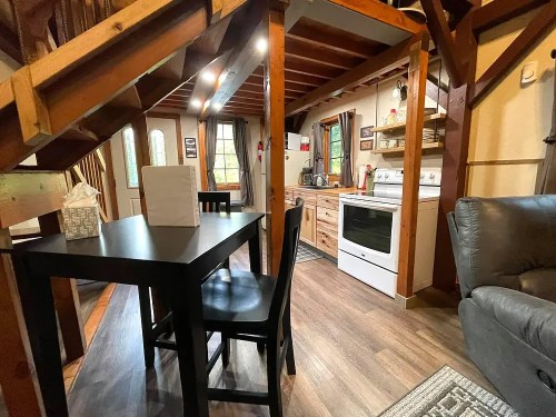 Cozy interior of a cabin featuring a kitchen, dining table, and living area with wooden beams and warm lighting.