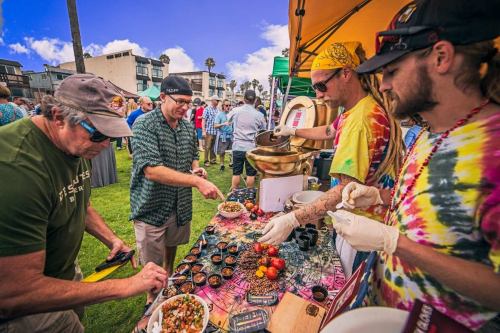 People sampling food at a vibrant outdoor market, with colorful tents and a lively crowd in the background.