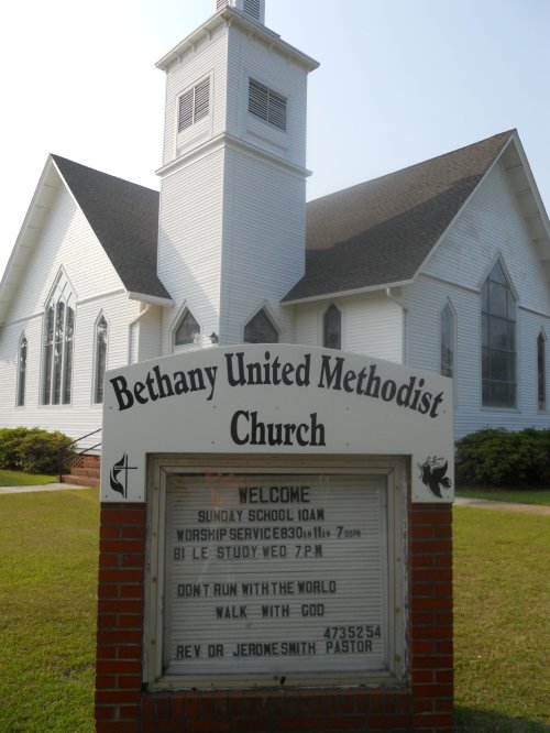A white church building with a steeple and a sign displaying service times and messages in front of it.