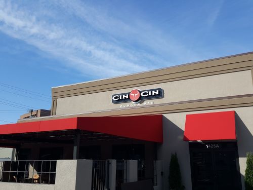 Exterior of Cin Cin Burger Bar with a red awning and clear blue sky in the background.