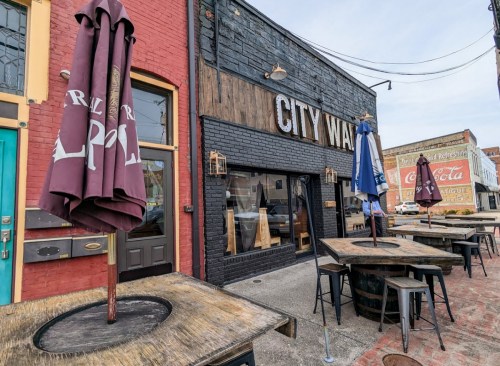 Exterior of a restaurant named "City Way," featuring outdoor seating and colorful umbrellas on a brick street.