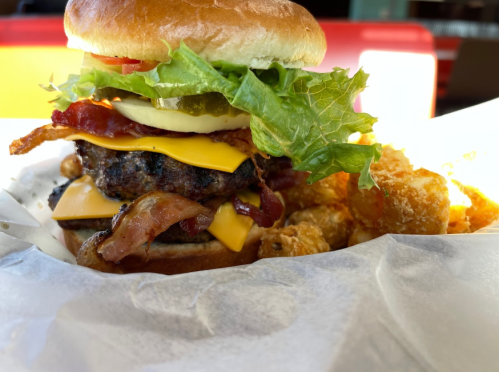 A juicy burger with lettuce, tomato, pickles, cheese, and bacon, served with crispy tater tots on the side.