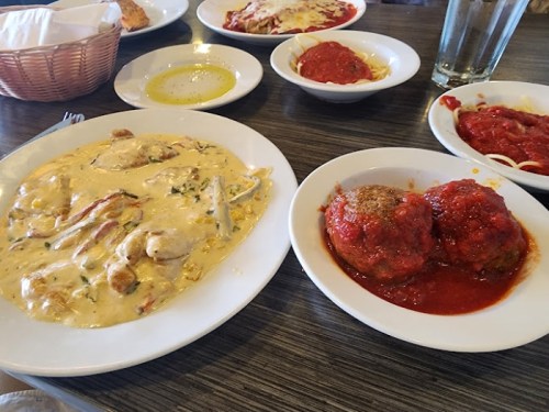 A table with two plates of food: creamy chicken dish and meatballs in tomato sauce, with sides and drinks in the background.