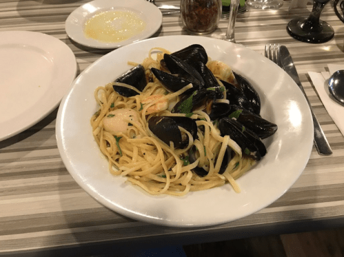 A plate of spaghetti with mussels and shrimp, garnished with herbs, served on a striped table.