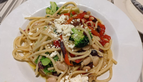 A plate of pasta with broccoli, red peppers, olives, and white beans, topped with crumbled feta cheese.