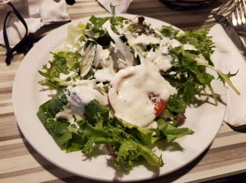 A plate of fresh salad topped with creamy dressing, featuring various greens and a slice of tomato.