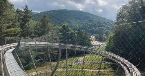 A winding track surrounded by a fence, set against a backdrop of green hills and a cloudy sky.