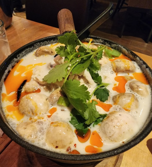 A bowl of creamy soup with meatballs, chicken, and fresh cilantro, garnished with orange oil swirls.
