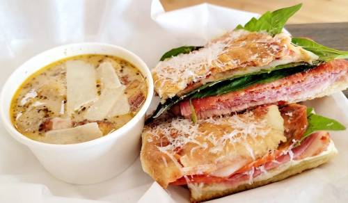 A sandwich with layers of meat and greens, served with a cup of creamy soup topped with cheese.
