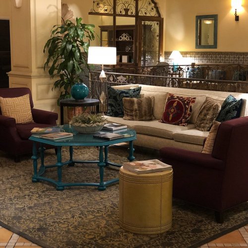 Cozy lounge area with a beige sofa, purple chairs, a blue coffee table, and decorative plants in a warm, inviting setting.