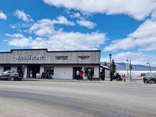 A waterfront building with signs for "Lakefront" and "Squatch Sweets," set against a cloudy blue sky and mountains.