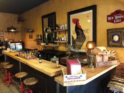 A cozy café interior featuring a wooden bar, shelves of drinks, and decorative items on the walls.