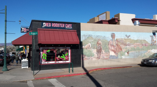 Exterior of Red Rooster Cafe featuring a mural and a sign for local beer, located at the corner of Pima Street.