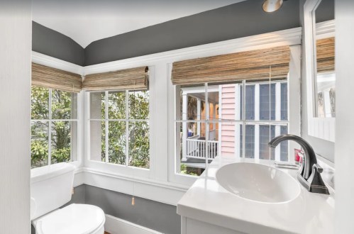 Bright bathroom with a modern sink, large windows, and natural light, featuring gray walls and bamboo shades.