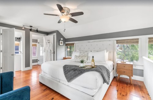 Bright, modern bedroom with a king bed, wooden floors, and large windows, featuring a cozy seating area and stylish decor.