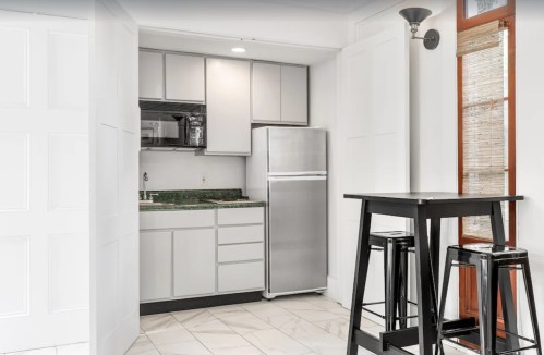 A modern kitchen with gray cabinets, a stainless steel fridge, and a small dining table with black stools.