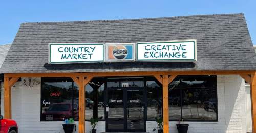 A storefront with a sign reading "Country Market" and "Creative Exchange," featuring a Pepsi logo and an "Open" sign.