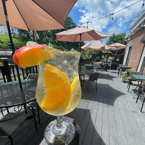 A refreshing drink with orange and apple slices sits on a table, surrounded by outdoor seating and umbrellas.