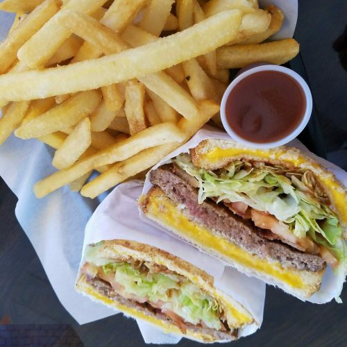 Two burgers with lettuce, tomato, and cheese, served with a side of golden fries and a small cup of dipping sauce.
