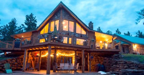 A cozy stone cabin with large windows, illuminated by warm lights, surrounded by trees at dusk.