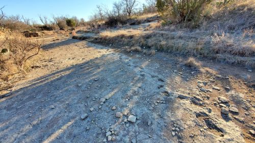 A dry, rocky landscape with sparse vegetation and a clear blue sky, showing signs of drought.