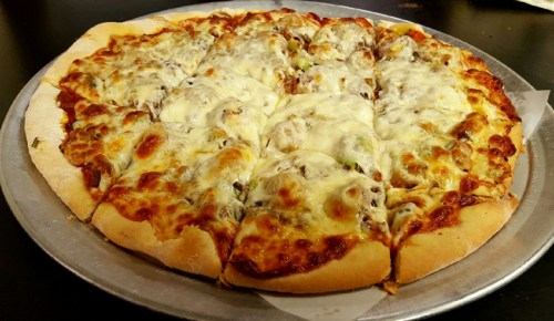 A freshly baked pizza with melted cheese, toppings, and sliced into equal pieces on a silver tray.