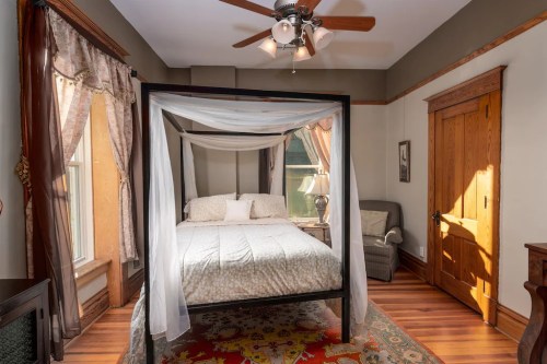 Cozy bedroom featuring a four-poster bed, armchair, and warm wooden accents with natural light from the windows.