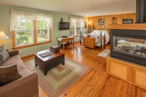 Cozy room with a bed, sofa, TV, and fireplace, featuring wooden accents and large windows with garden views.