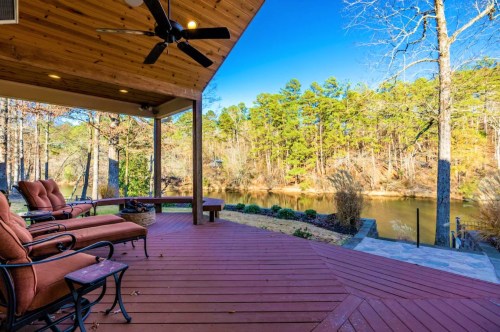 A cozy porch with seating overlooks a serene lake surrounded by trees under a clear blue sky.