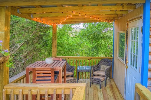 Cozy outdoor patio with wooden furniture, string lights, and lush greenery in the background.