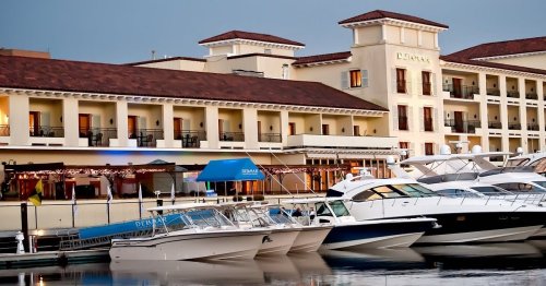 A marina with luxury yachts docked in front of a stylish hotel at sunset.
