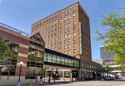 A tall brick building with large windows, connected to a modern glass structure, set against a clear blue sky.