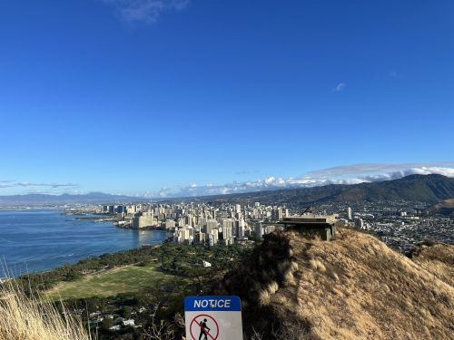 A panoramic view of a city skyline by the coast, with mountains in the background and a clear blue sky.