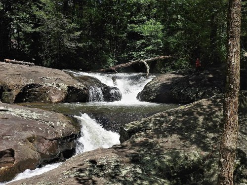 A serene waterfall cascades over rocky terrain, surrounded by lush green trees in a peaceful natural setting.