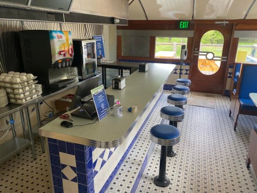 A retro diner interior featuring a counter with stools, a drink station, and tiled flooring.
