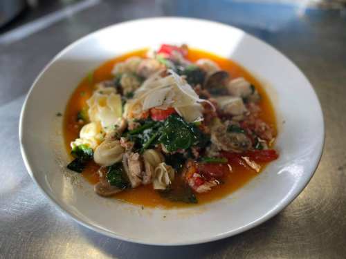 A plate of pasta with seafood, spinach, tomatoes, and cheese in a rich orange sauce, garnished and ready to serve.