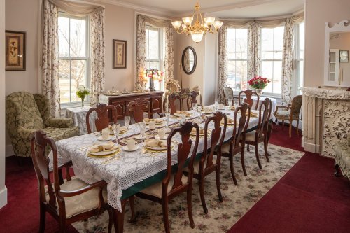 A beautifully set dining room with a long table, elegant chairs, and large windows, adorned with floral decor.