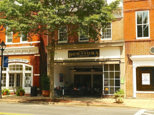 A brick building with a sign reading "Doc's Downtown Grille," featuring outdoor seating and large windows.