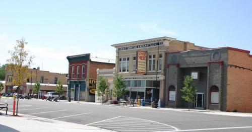 A sunny street view of a small town with historic buildings, shops, and trees lining the sidewalk.