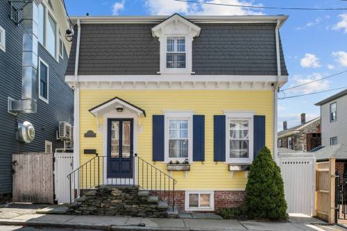 A charming yellow house with blue shutters and a stone staircase, set against a clear blue sky.