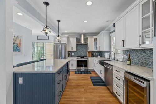 Modern kitchen with white cabinets, blue accents, stainless steel appliances, and a large island with a wooden floor.