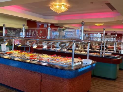 A brightly lit buffet with various food options displayed in trays under glass covers.